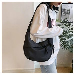 Detail of minimalist black nylon half-moon crossbody bag with adjustable wide strap on model