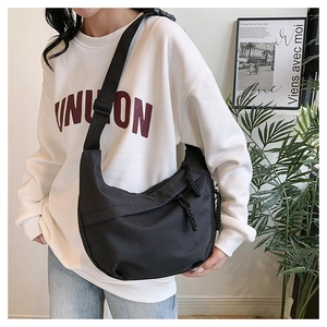 Detail of adjustable strap and knot zipper on black crescent crossbody bag worn by model