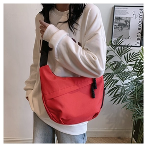 Detail of red crescent nylon crossbody bag with wide black strap on a white hoodie