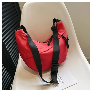 Detail of red crescent shoulder bag featuring adjustable black strap on white chair