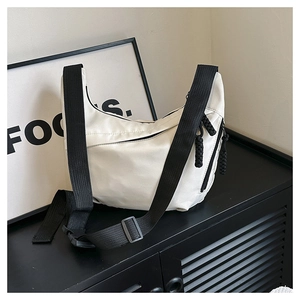 Detail of a beige crescent crossbody bag with adjustable black strap on a display shelf