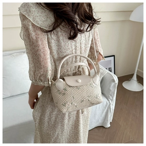 Detail of woven beige bag with delicate floral embroidery and leather flap