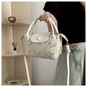 Détail d'un sac à main en paille tressée avec broderie florale et garniture blanche