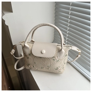 Detail of beige straw handbag with floral embroidery and adjustable crossbody strap