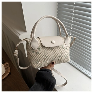 Detail of beige woven handbag with delicate pink and green floral embroidery and round handles