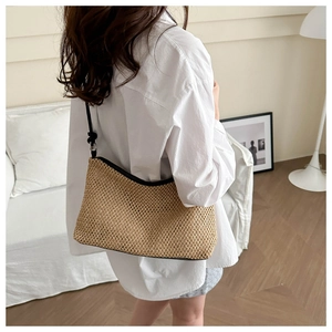 Detail of woven straw shoulder bag with black trim and slim strap on model