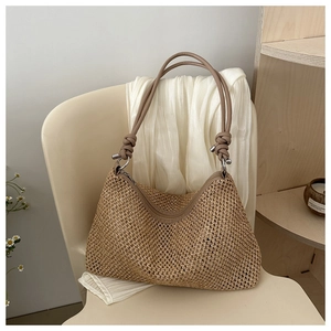 Detail of woven straw tote bag featuring knot handle design and silver metal rings