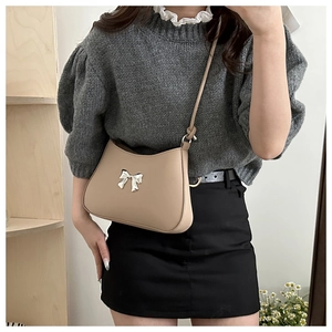 Detail of a beige crossbody bag with a golden bow buckle and fine leather texture