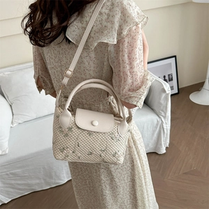 Beige woven handbag with floral embroidery and adjustable strap in home setting