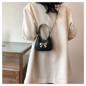 Detail of a black mini bag with silver metal bow and fine chain strap on a white blazer