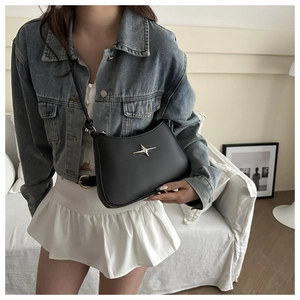 Close-up of black leather crossbody bag with silver star emblem worn by a model