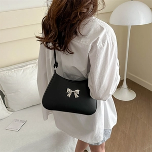 Borsa a tracolla minimalista in pelle nera opaca con fiocco argento su sfondo crema