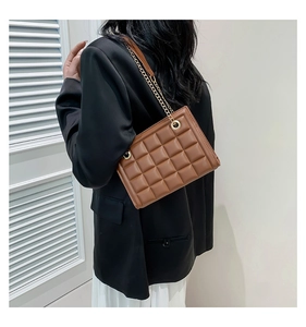 Détail du sac matelassé marron avec bandoulière en chaîne dorée porté par un modèle