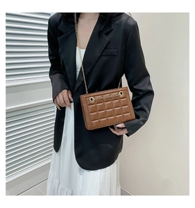 Détail d'un sac à bandoulière matelassé marron avec chaîne dorée porté sur un blazer noir