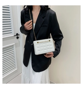 Sac bandoulière blanc matelassé avec chaîne dorée porté par un mannequin en blazer noir
