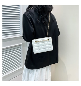 Détail d'un sac à bandoulière matelassé blanc avec chaîne dorée porté par un modèle