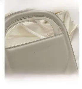 Detail of white faux leather handbag featuring a unique semi-circle cutout handle and stitching