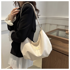 Détail du sac hobo minimaliste en cuir crème avec écusson rectangulaire sur un mannequin