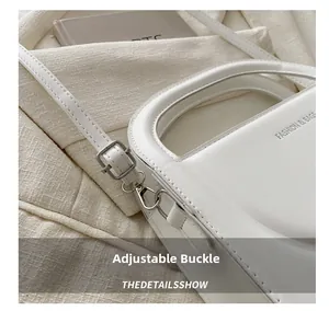 Detail of adjustable metal buckle and contrast stitching on white faux leather bag