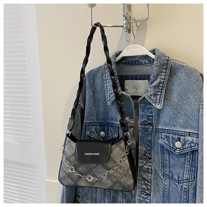 Gros plan du sac à bandoulière gris matelassé avec chaîne florale argentée sur veste en jean