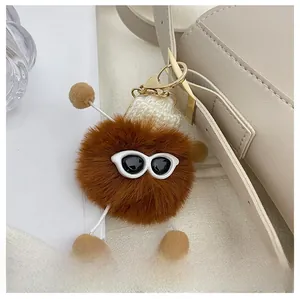 Dettaglio di un ciondolo in peluche con occhiali e cappello su una borsa in pelle beige