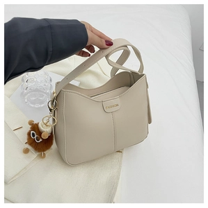 Dettaglio borsa hobo in pelle PU beige con targa dorata e ciondolo a forma di orso