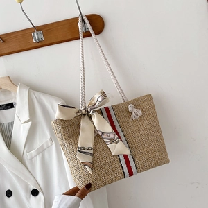 Detail of woven straw tote bag featuring decorative silk bow and striped cotton rope handle