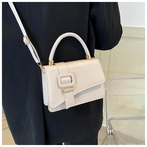 Dettaglio borsa a tracolla bianco avorio con fibbia dorata su sfondo blazer nero