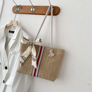 Detail of a woven straw tote with white rope handles and red striped ribbon accent
