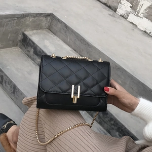 Detailed close-up of black quilted chain bag with gold metal clasp on a gray background