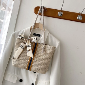 Detail of hand-woven straw tote with colorful stripes and silk scarf on wooden hanger