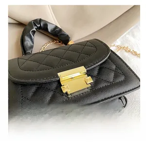 Detail of black quilted shoulder bag featuring gold square clasp and ruched fabric handle