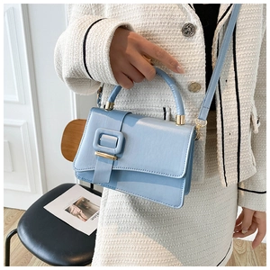 Dettaglio borsa a mano in pelle PU celeste con finiture dorate su abito in tweed