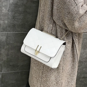 White quilted flap bag with golden chain strap and lock closure on tweed coat