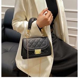 Detail of black quilted shoulder bag with gold metal lock and chain strap on model