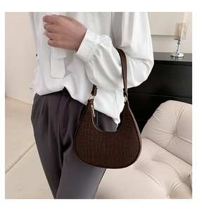 Detail of dark brown faux crocodile leather underarm bag on a model in a modern home setting