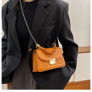 Detail of orange quilted crossbody bag with gold chain strap worn with black blazer