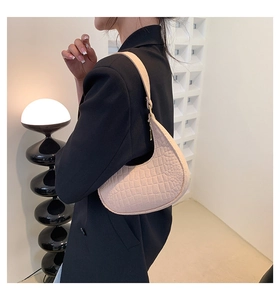 Detail of beige crocodile pattern crescent bag worn over the shoulder by a model