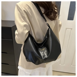 Détail du sac bandoulière en cuir noir avec plis souples et étiquette logo de la marque