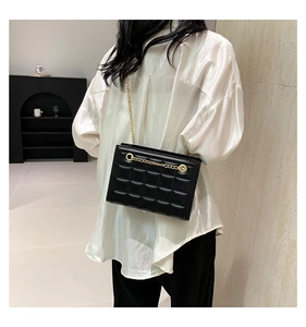 Détail d'un sac matelassé noir avec chaîne dorée porté par un mannequin à l'épaule