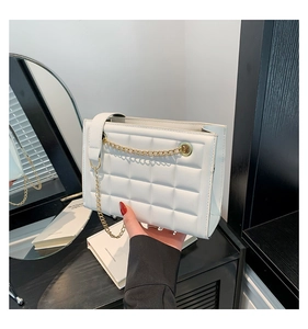 Gros plan sur le sac matelassé blanc avec chaîne dorée posé sur une étagère moderne