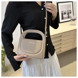 Close-up of a beige faux leather handbag with silver lettering and adjustable strap