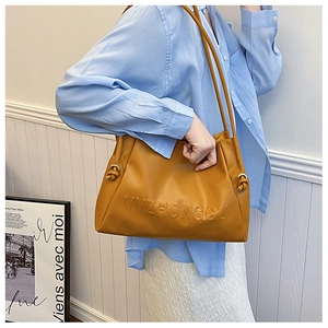 Detalle del bolso tote amarillo en cuero sintético con logo grabado y nudo de cordón lateral