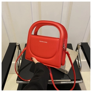 Detail of red crossbody bag with curved flap and Fashion text on a black chair
