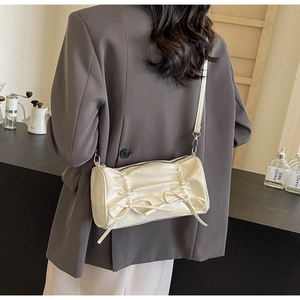 Close-up of cream pleated cylinder bag with decorative bows worn by a model in a cafe