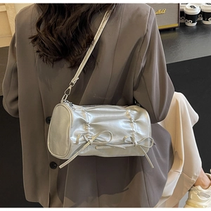 Detail of silver pleated cylindrical crossbody bag with cute bows on a female model