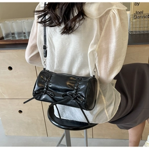 Detail of black cylindrical pleated shoulder bag featuring double bow accents and silver buckles