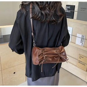 Detail of coffee brown pleated cylindrical bag with fringe drawstring and adjustable strap