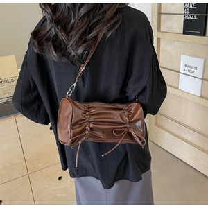 Detail of a dark brown pleated cylindrical crossbody bag with dainty bow decorations
