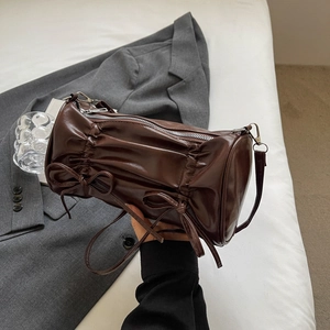 Detail of dark brown pleated cylinder bag with bows and silver zipper closure